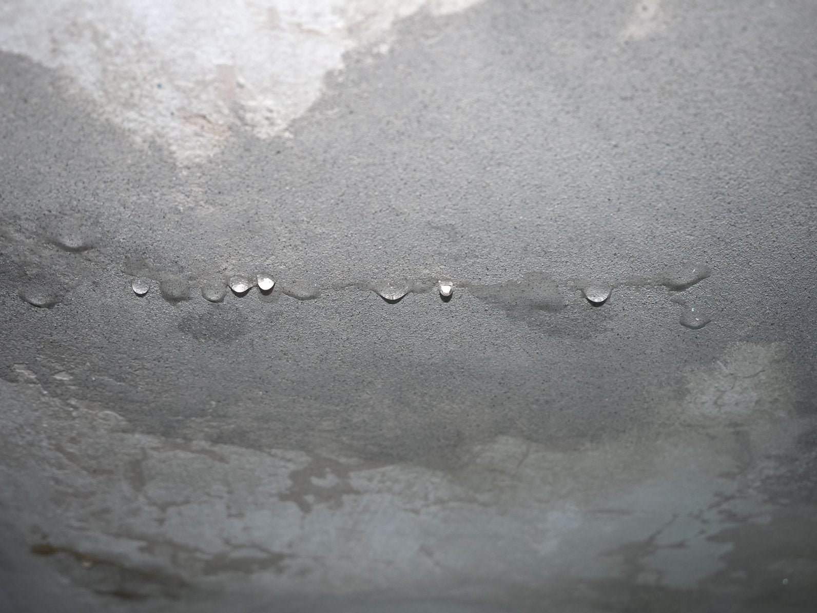 Water droplets beading on a damp, stained ceiling